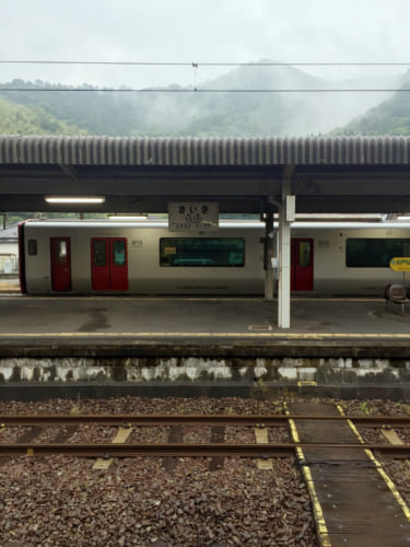 Train dans la gare de Saiki, devant un paysage de montagnes embrumées
