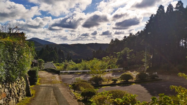 Tano Kansa - landscape of the mountains in distance with shrubs and a road ahead.