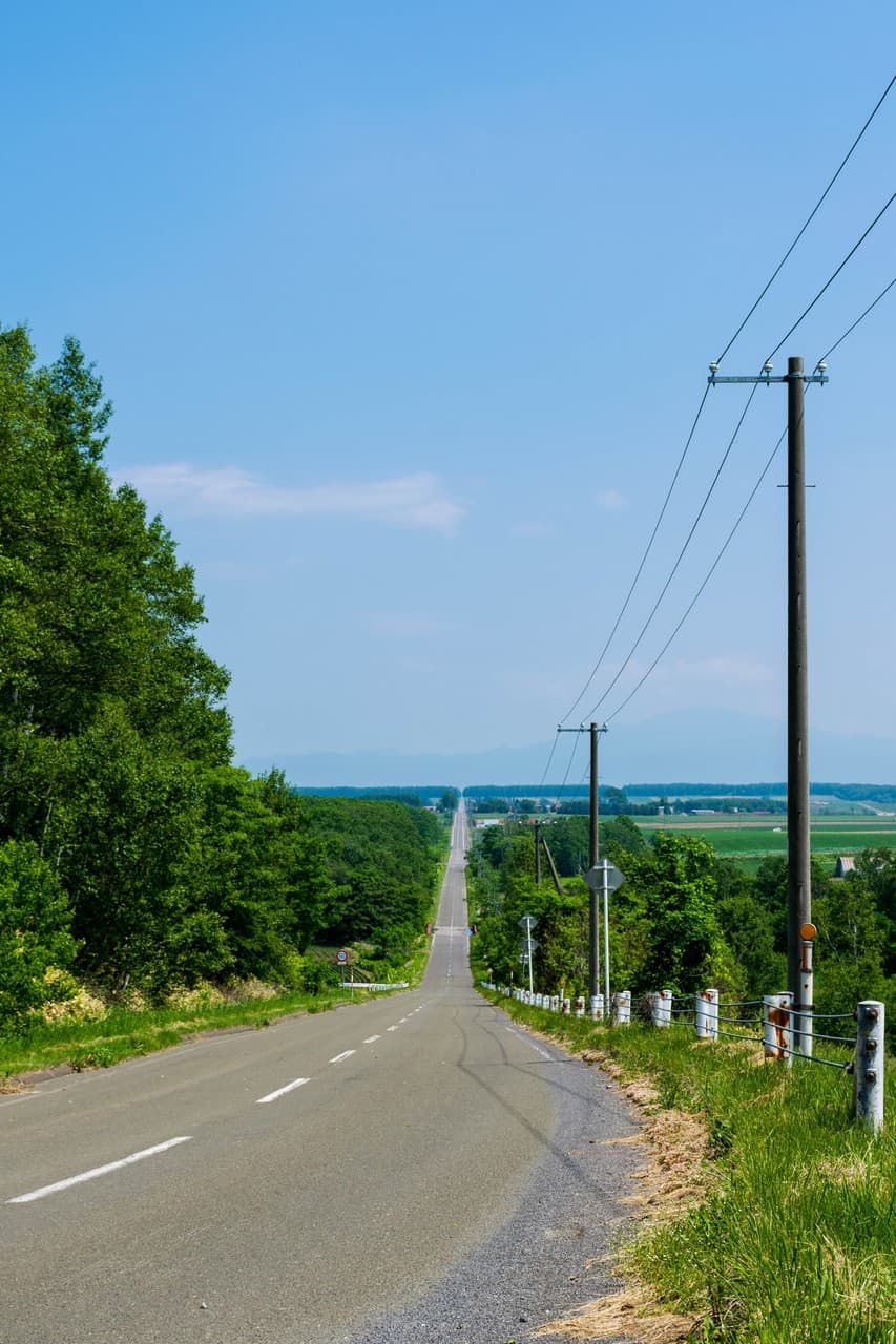 open road leading to rural landscape blue sky in hokkaido, japan