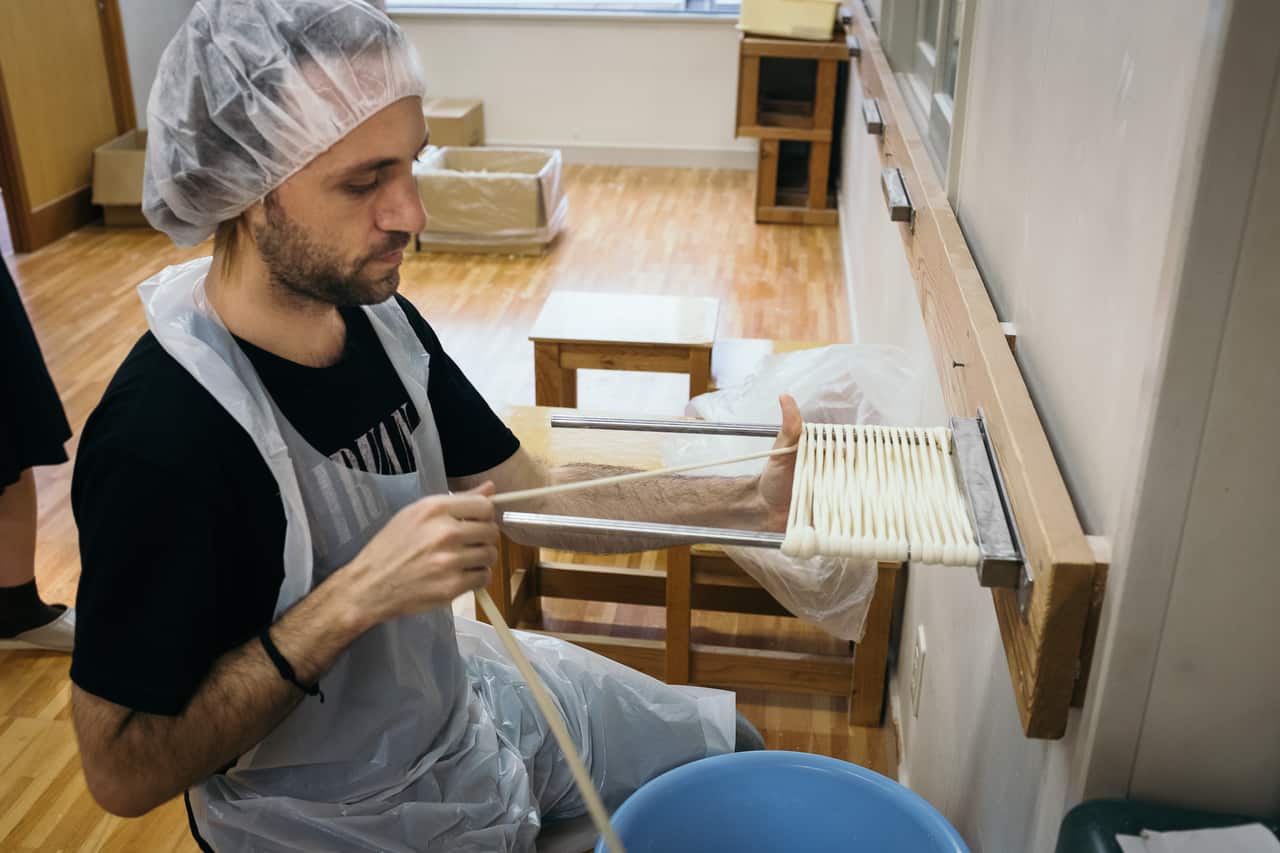 man in hair net pulling udon to prepare it for eating