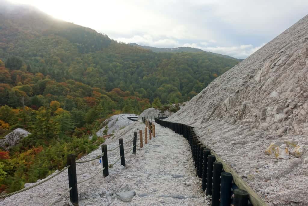 A white stone path of the jigoku kawarage extends towards the horizon in the middle of the green mountains of Akita Prefecture