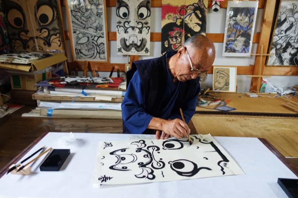 A craftsman painting the outlines of a character on a traditional kite in his workshop in Yuzawa, Akita Prefecture