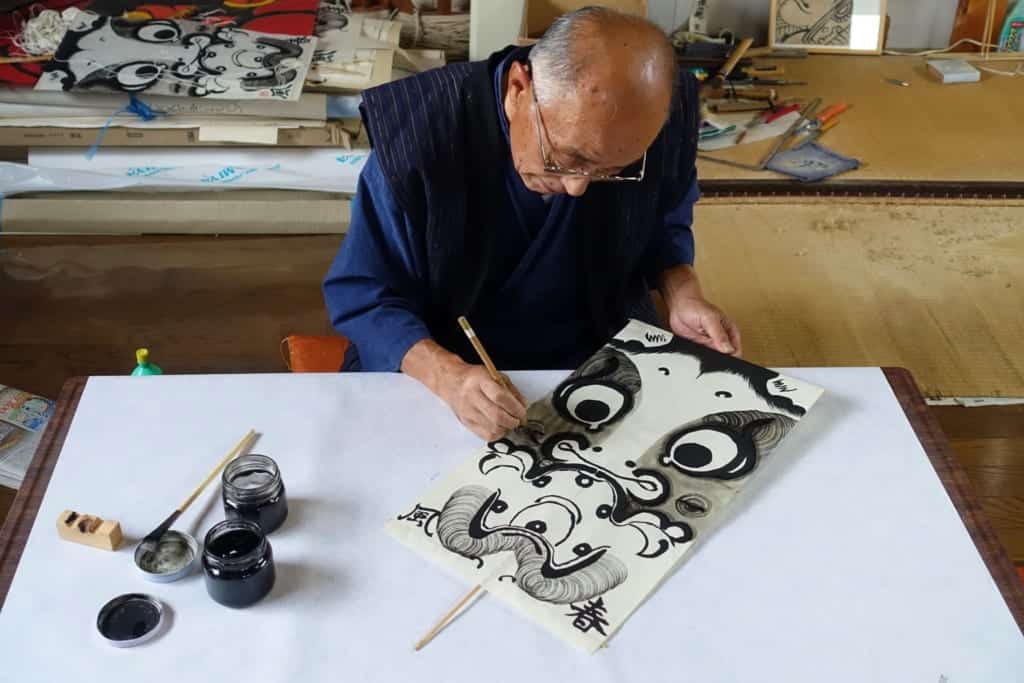 Mr. Ono, carefully drawing the design of his kite in black ink
