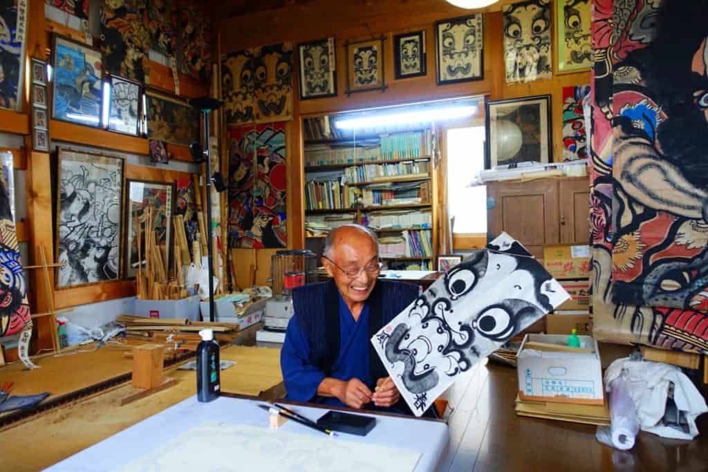 Mr. Ono smiling, posing with his finished kite in his workshop in Yuzawa, Akita Prefecture