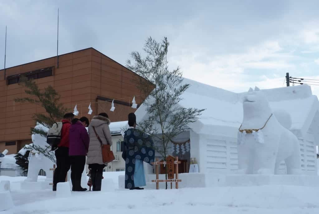 Japanese meditating in front of a temple carved in snow for the Inukko Matsuri festival
