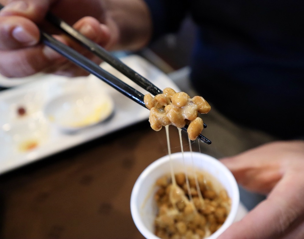 person's hands holding chopsticks and natto fermented Japanese food