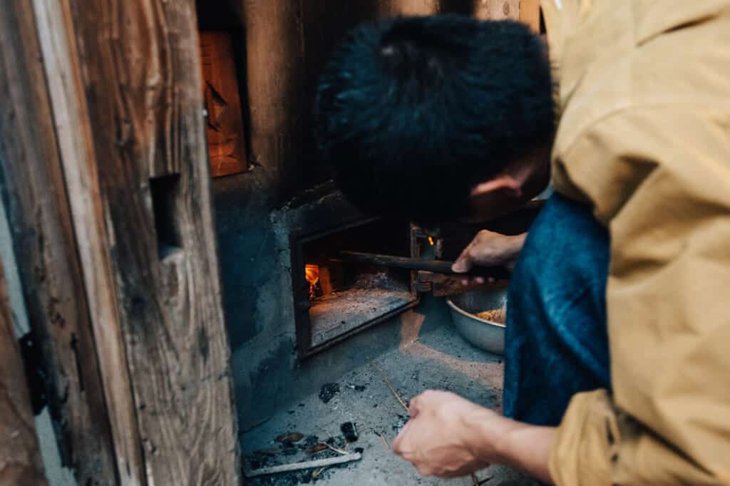 Lighting a fire under fire-heated ofuro (bath) at Yanoya guesthouse on Ojika Island