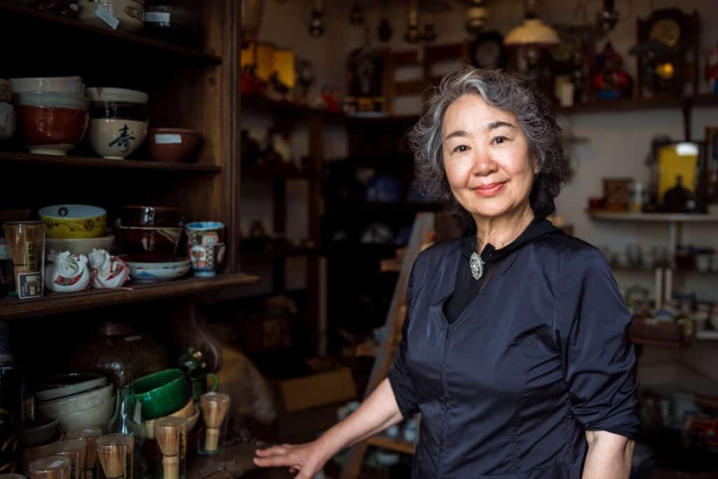 Smiling Japanese woman standing in her antiques shop in Joge town