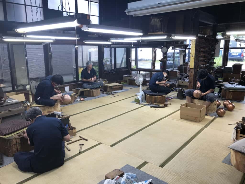 Japanese craftsmen crafting metal tea pots in a traditional tatami room. 