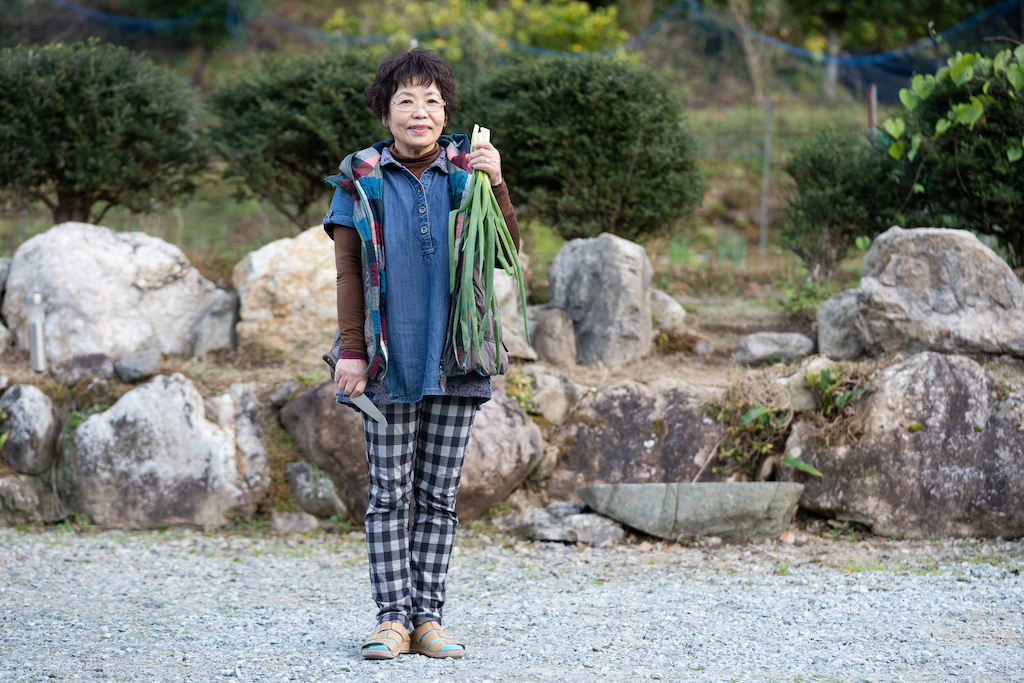 Mrs. Ogura holds fresh spring onions in front of the garden