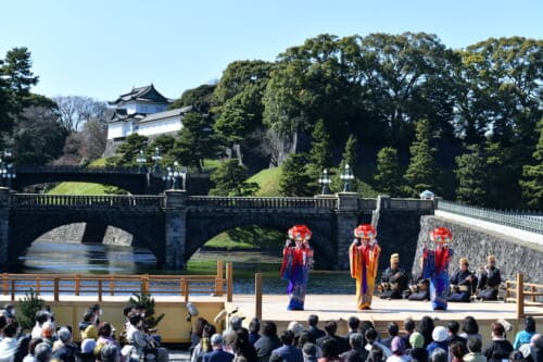 Three dancers on stage in front of a bridge and Imperial Palace