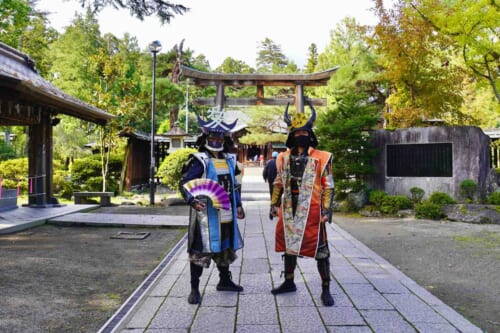 2 men dressed as samurai in front of shrine