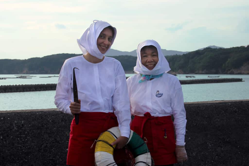 two women pose as ama divers in white blouses and hats.