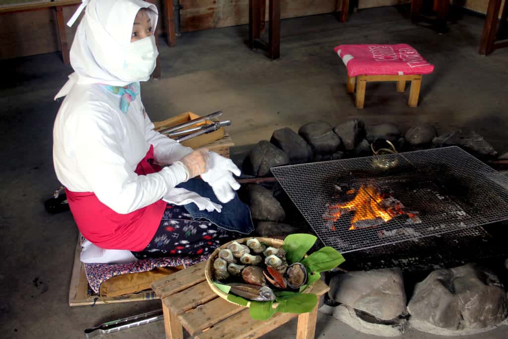 an ama diver is sitting next to a fire, ready to prepare the seafood she caught earlier