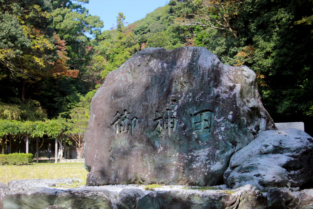a rock standing in front the the rice with engraved kanji 