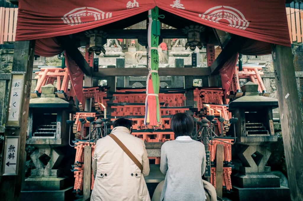 Two Japanese praying in front of a Shinto altar