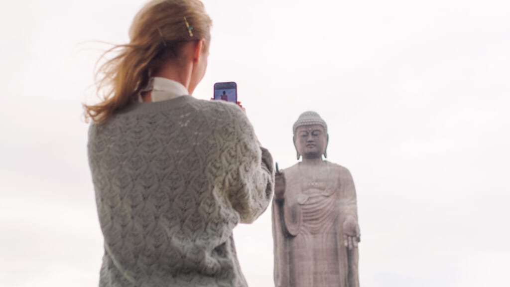 woman taking photo of ushiku daibutsu Buddha statue in  japan