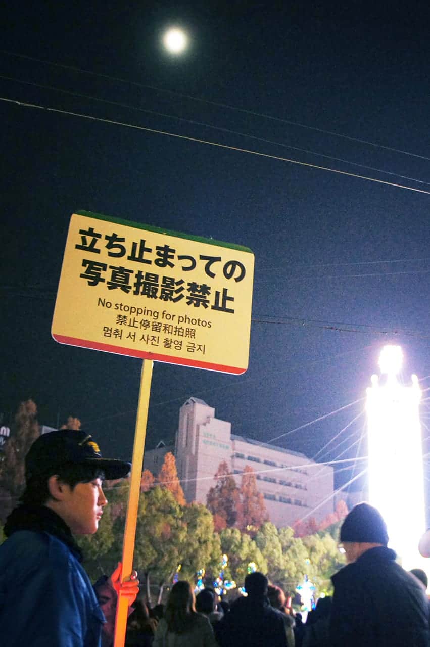 young Japanese person holding a sign: “No stopping for photos”