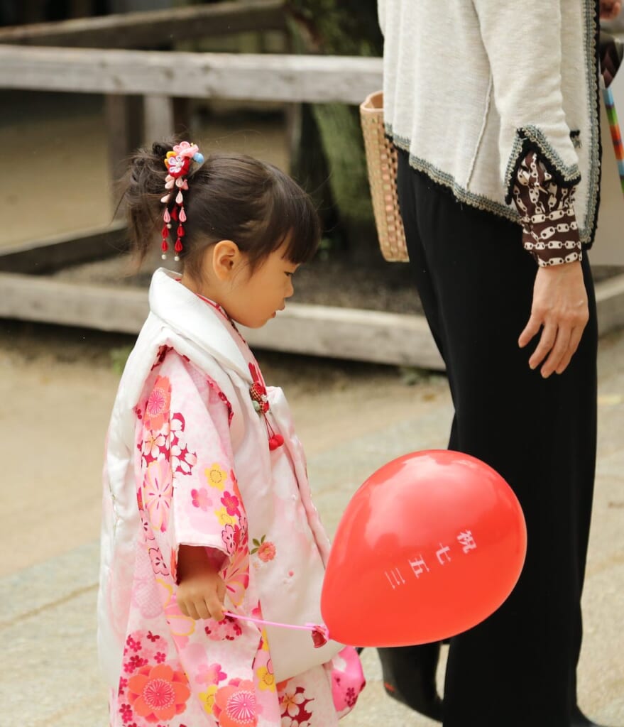 little girl in pink kimono holding a balloon in japan