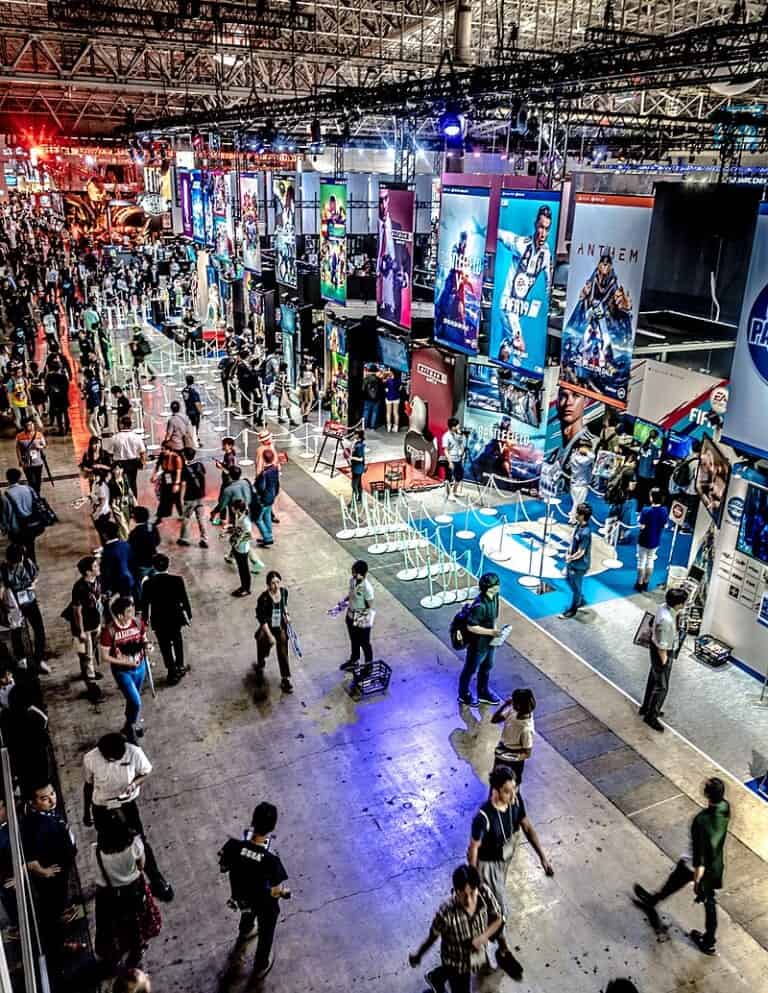 People walking around large stadium at Tokyo GAme Show with video game posters having from ceiling
