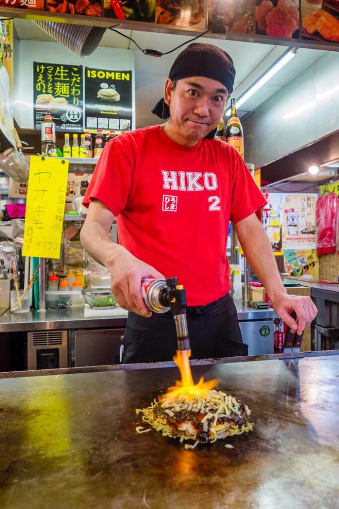 Japanese man blow torching Osaka's famous okonomiyaki dish on hot plate