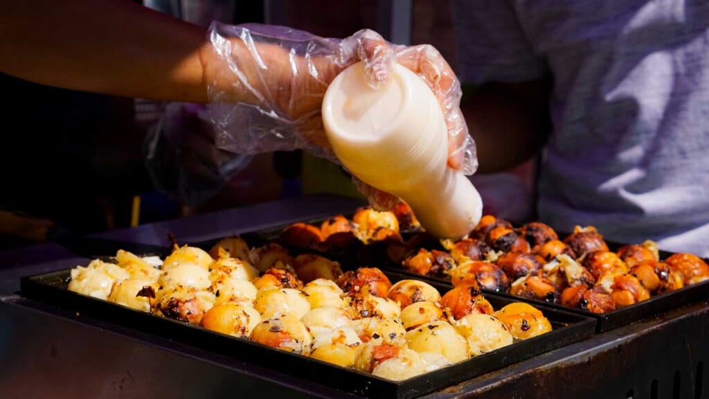 close up of tray of cooking takoyaki, Japan's famous street food of battered balls with octopus in the center