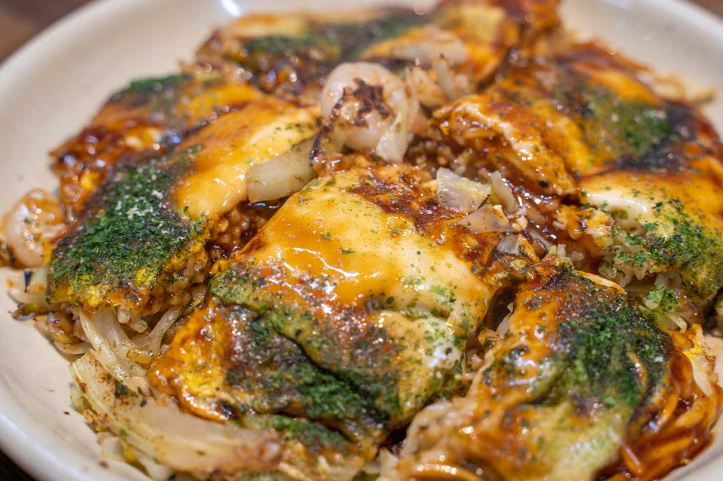 close up of hiroshima-style okonomiyaki dish with noodles and green seaweed