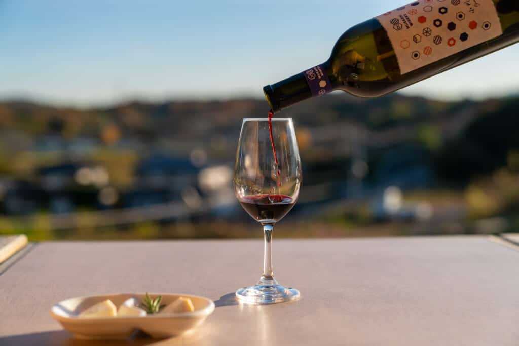 Japanese red Musashi Wine being poured into a glass against a beautiful natural backdrop 