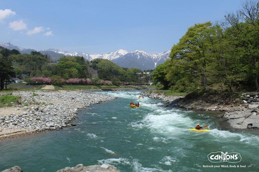 people in raft in a river with japanese alps in the background