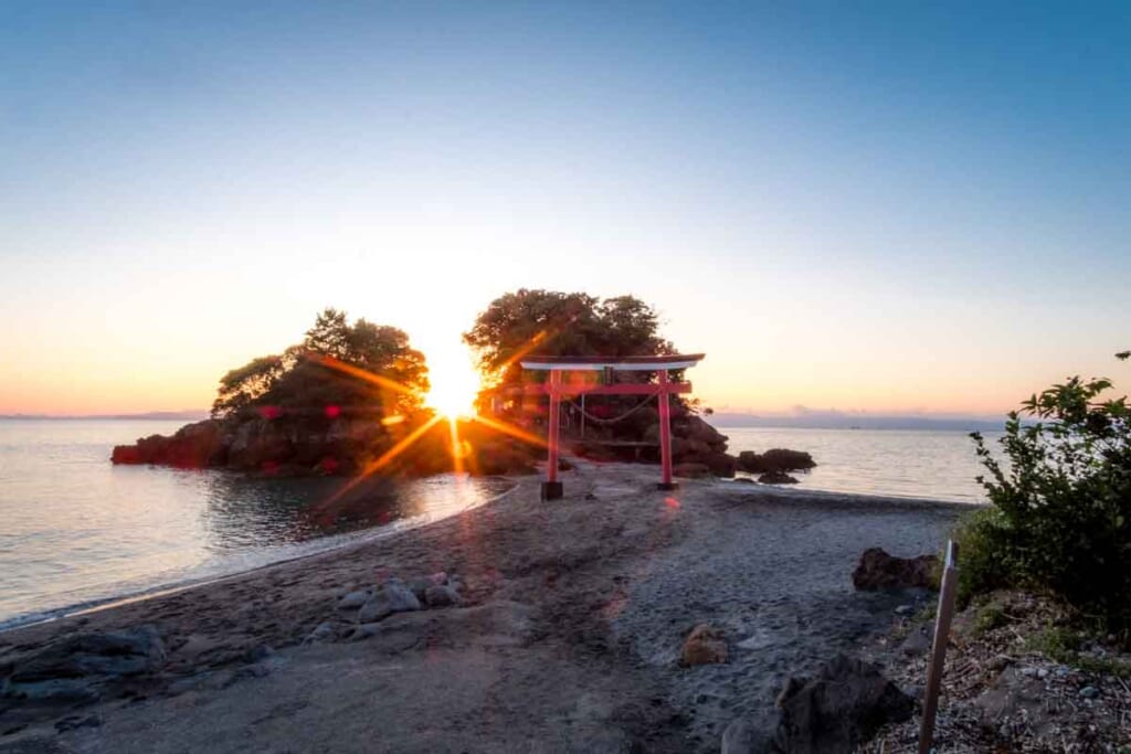 sun sets behind small island and torii gate at Sugawara Shrine in Kagoshima, Japan