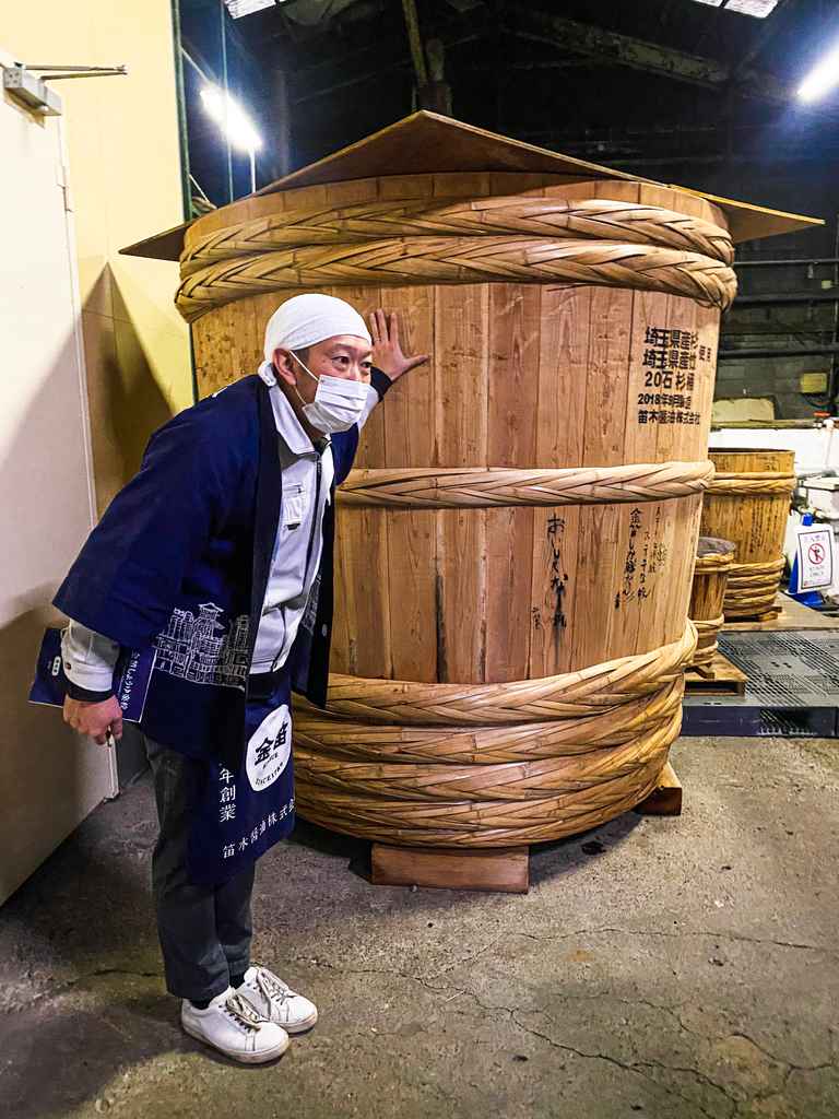 man standing next to giant soy sauce barrel in japan