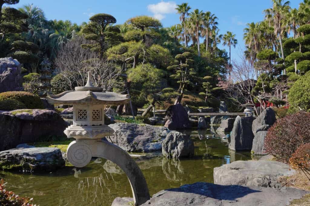Japanese style garden and stone lantern, with palm trees in the distance, Amami no Sato