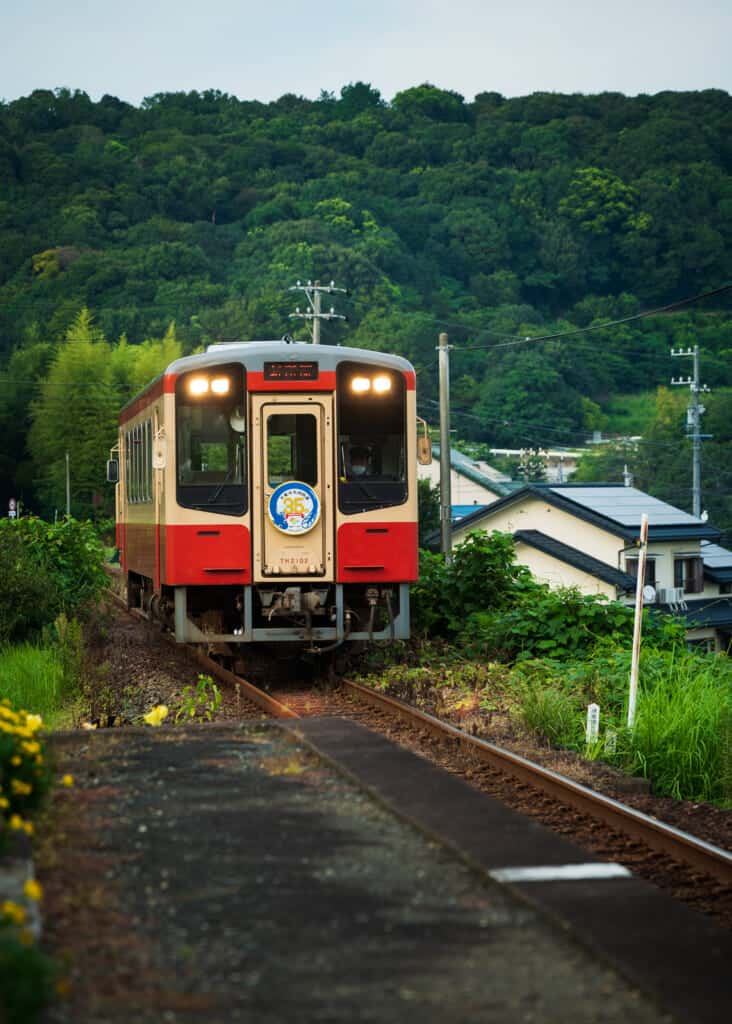  a red and  yellow tenhama line train in hamamatsu japan, with forest background