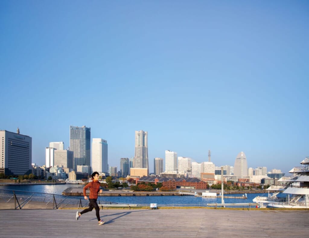 A jogger running along Yokohama Port with the city skyline in the background.