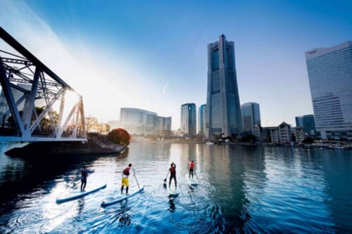 People doing stand up paddle boarding in Yokohama Bay with a view of the city in the background.