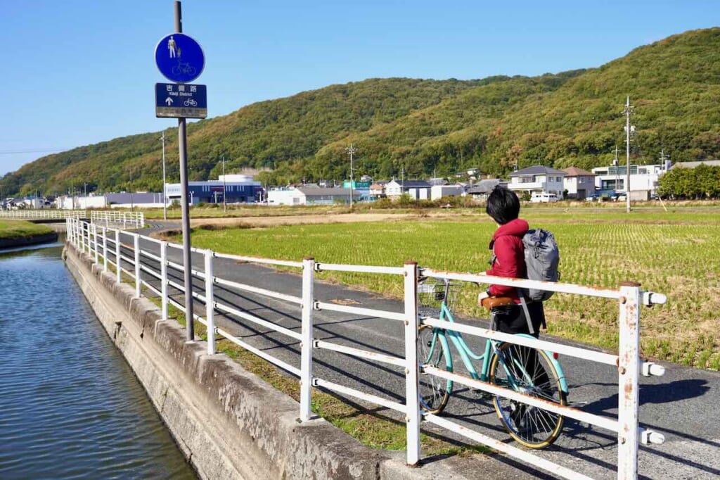 Person with bicycle in rural setting looking at Kibiji route sign