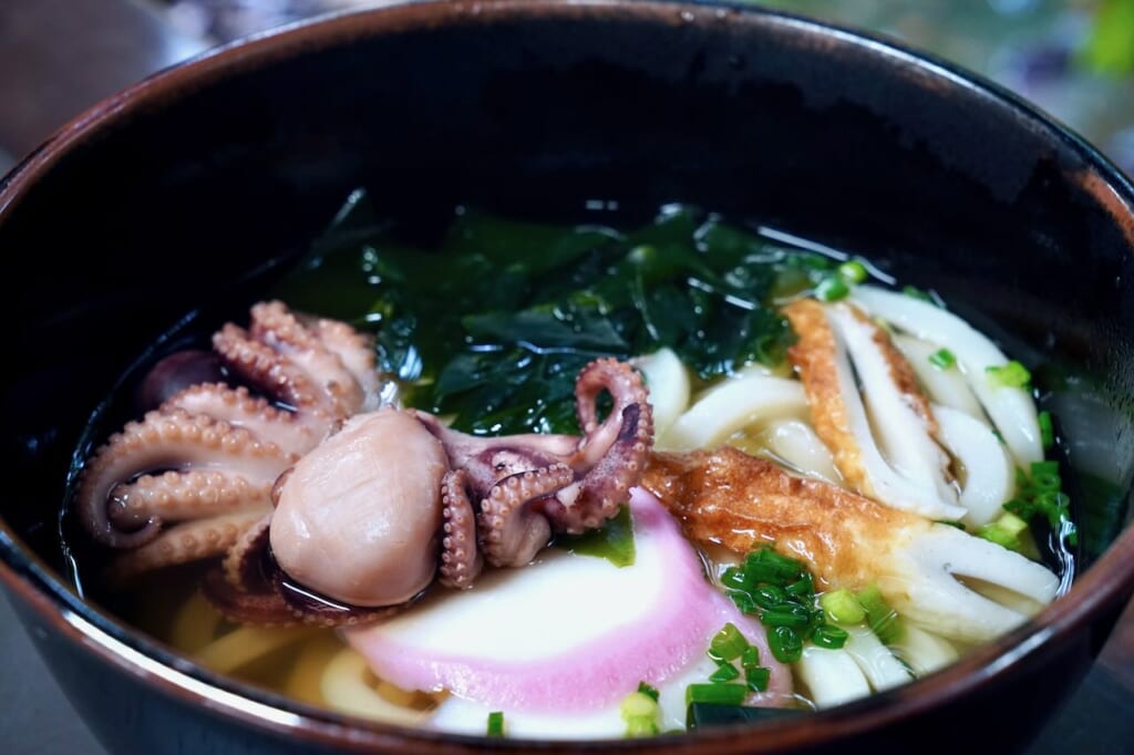 bowl of udon with baby octopus, wakame, fish cakes