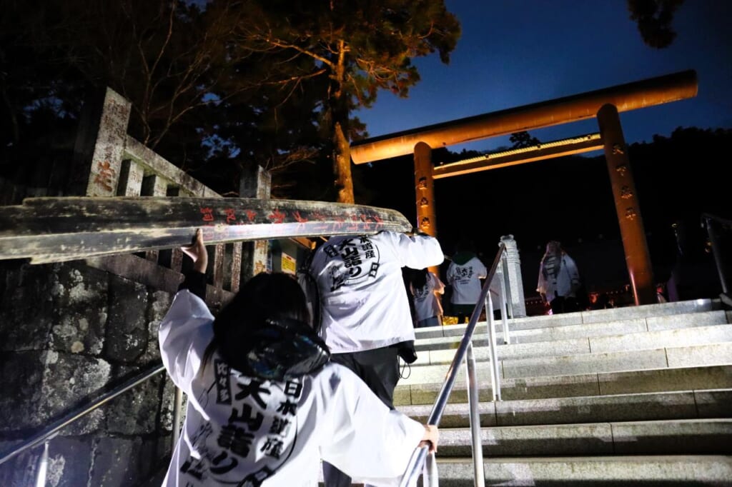 2 people carrying the wooden sword osamedachi up steps to shrine