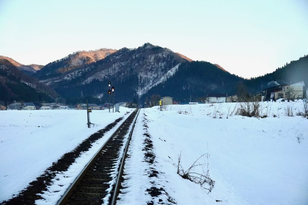 Railway going through snowscape headed straight into mountains as seen from Smile Rail train in Akita