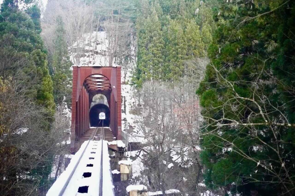 Railway bridge and tunnel surrounded by snowy forest as seen from Smile Rail train in Akita