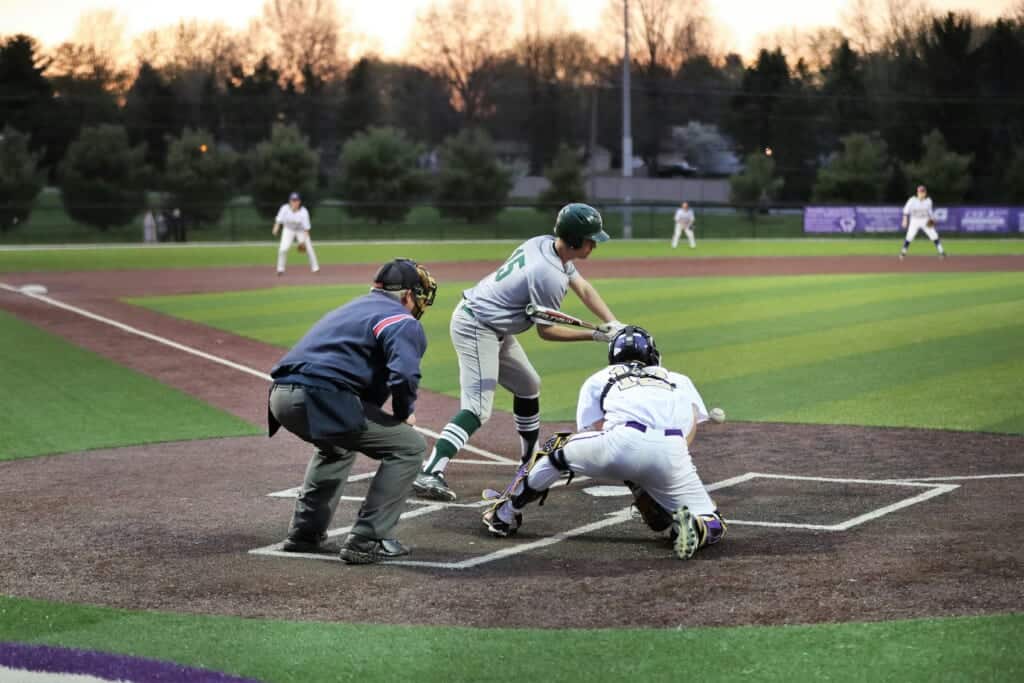 baseball player hitting ball with catcher behind him with green field