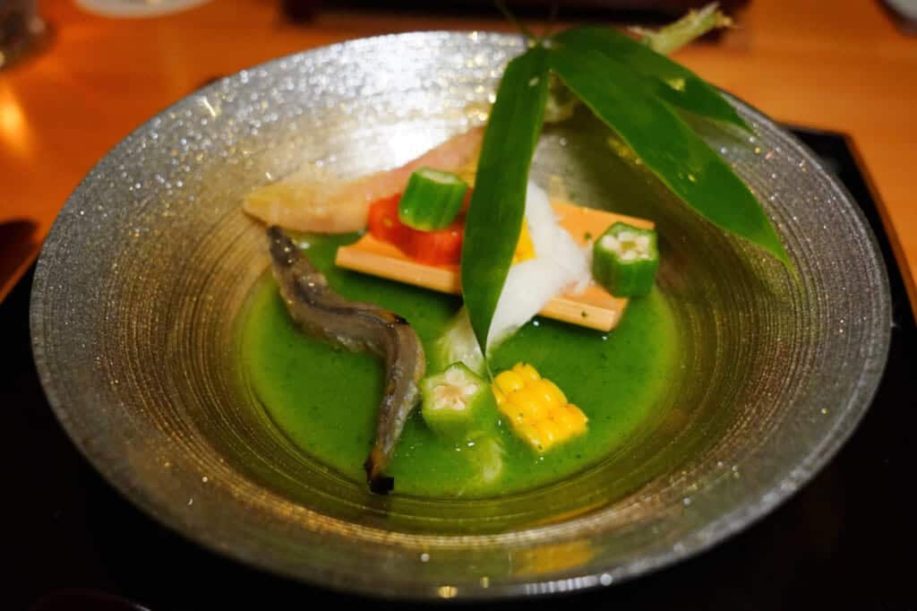 A grey bowl with a green soup, fish, and vegetables