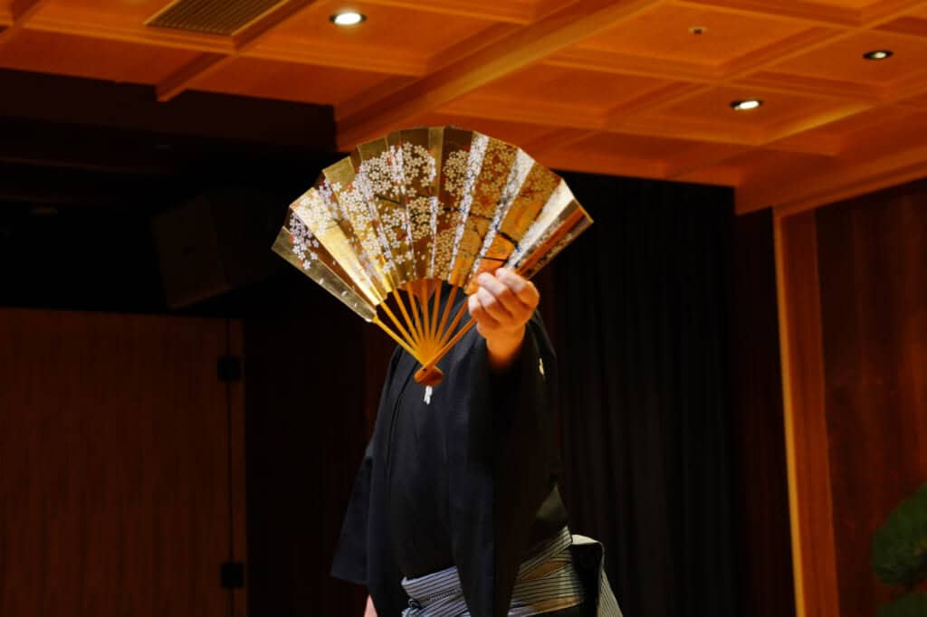 A man covering his face with a golden fan decorated with cherry blossoms