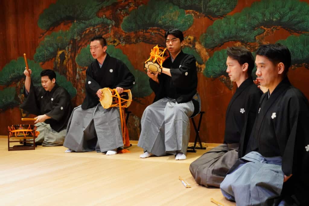 Five men on a Japanese stage, three holding Japanese drums