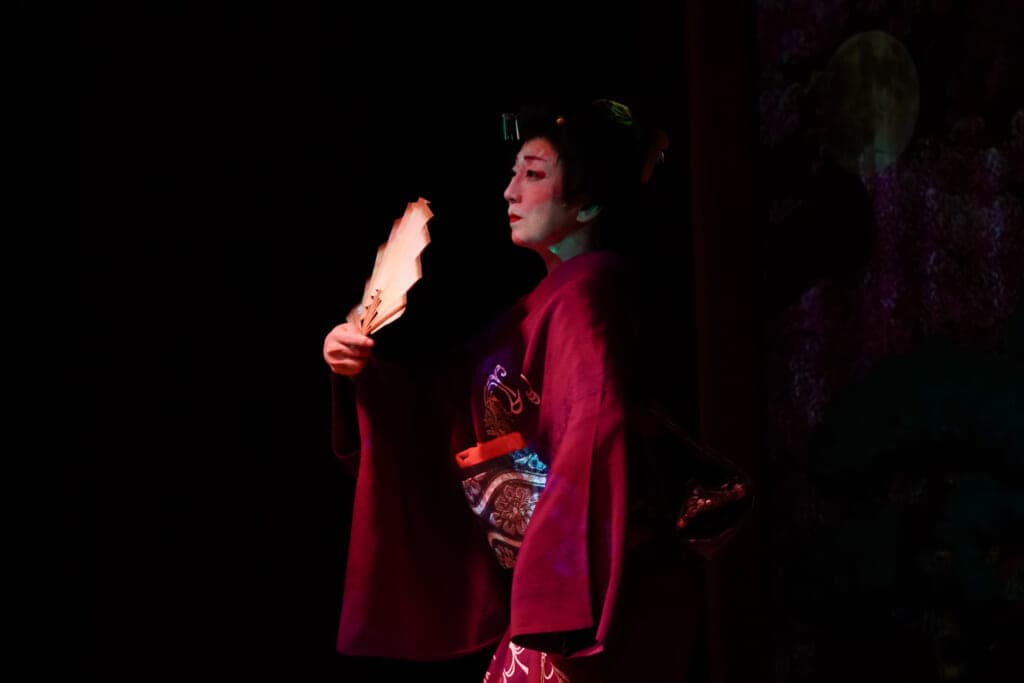 A woman in white make up and a kimono against a dark background