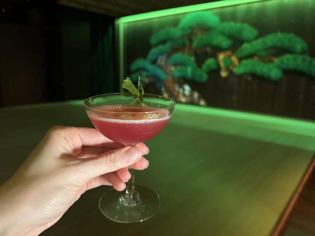 A pink cocktail being held in front of a Noh stage