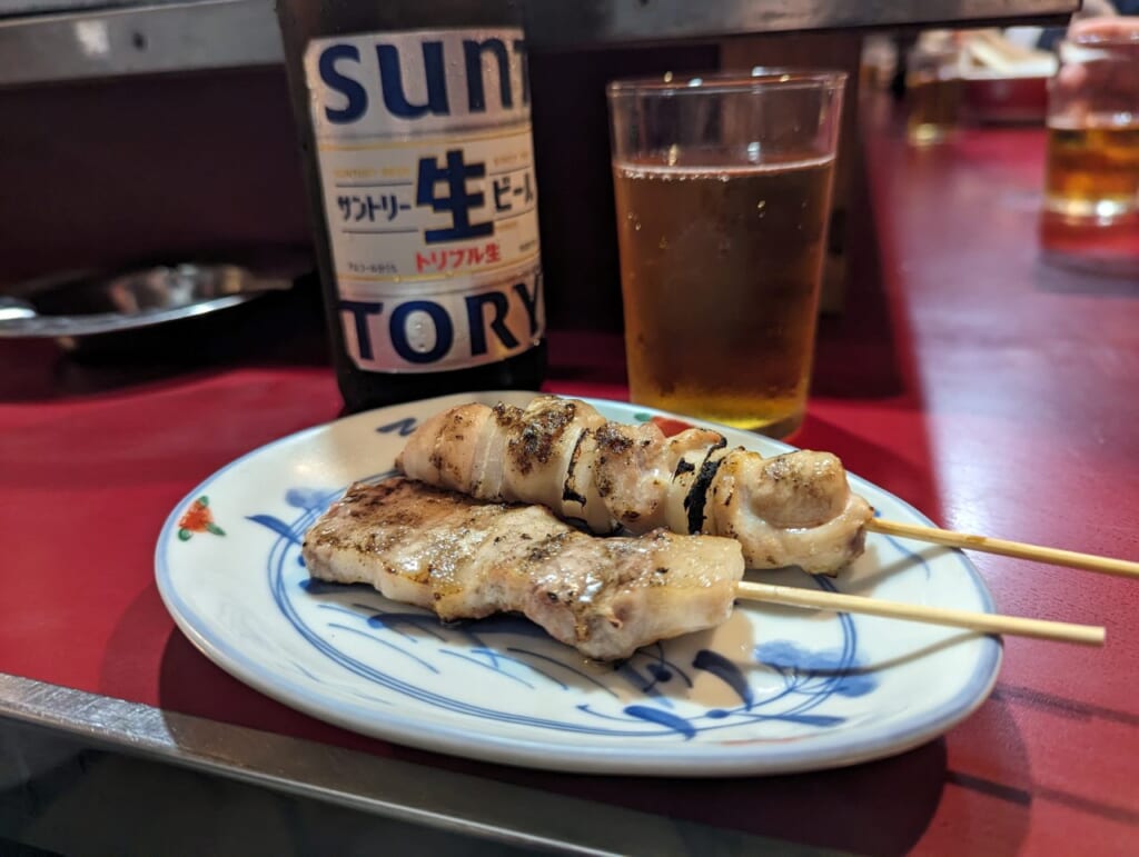 Yakitori on a blue and white plate with a bottle of beer behind it.