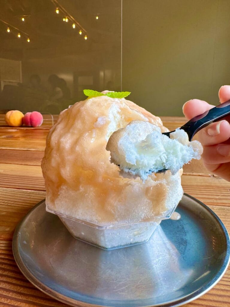 A woman's hand holding a spoonful of kakigori shaved ice in front of the plate