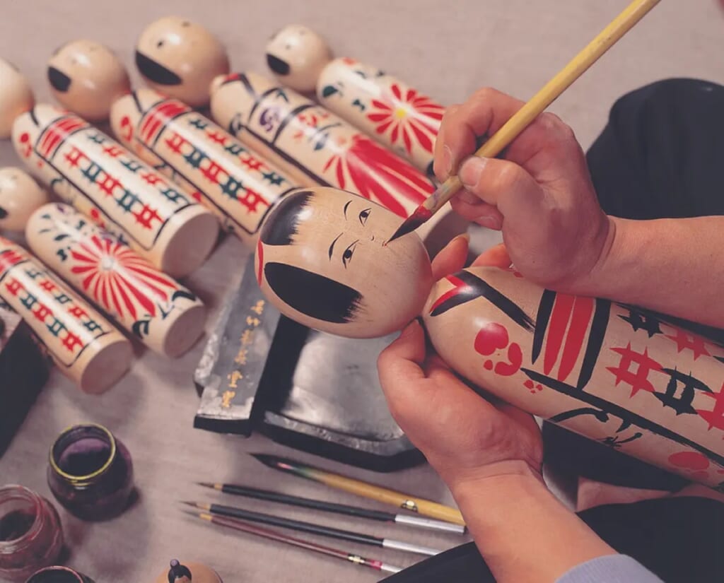 person painting a japanese kokeshi doll