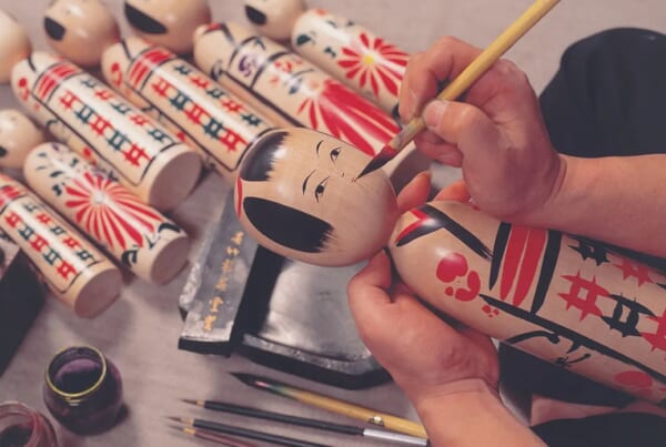 person painting a japanese kokeshi doll